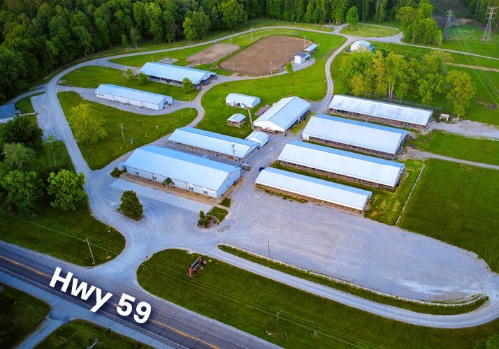 Aerial view of a rural business complex with white-roofed buildings beside Hwy 59 and trees.