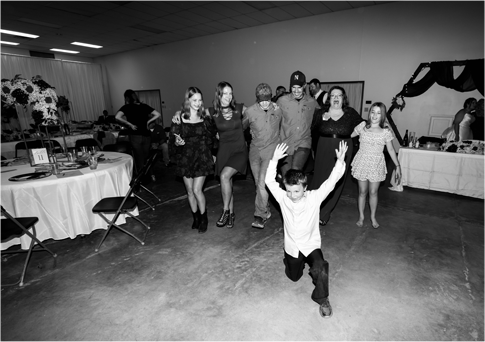 Guests dance at a party in a banquet hall, with a child running in the foreground.