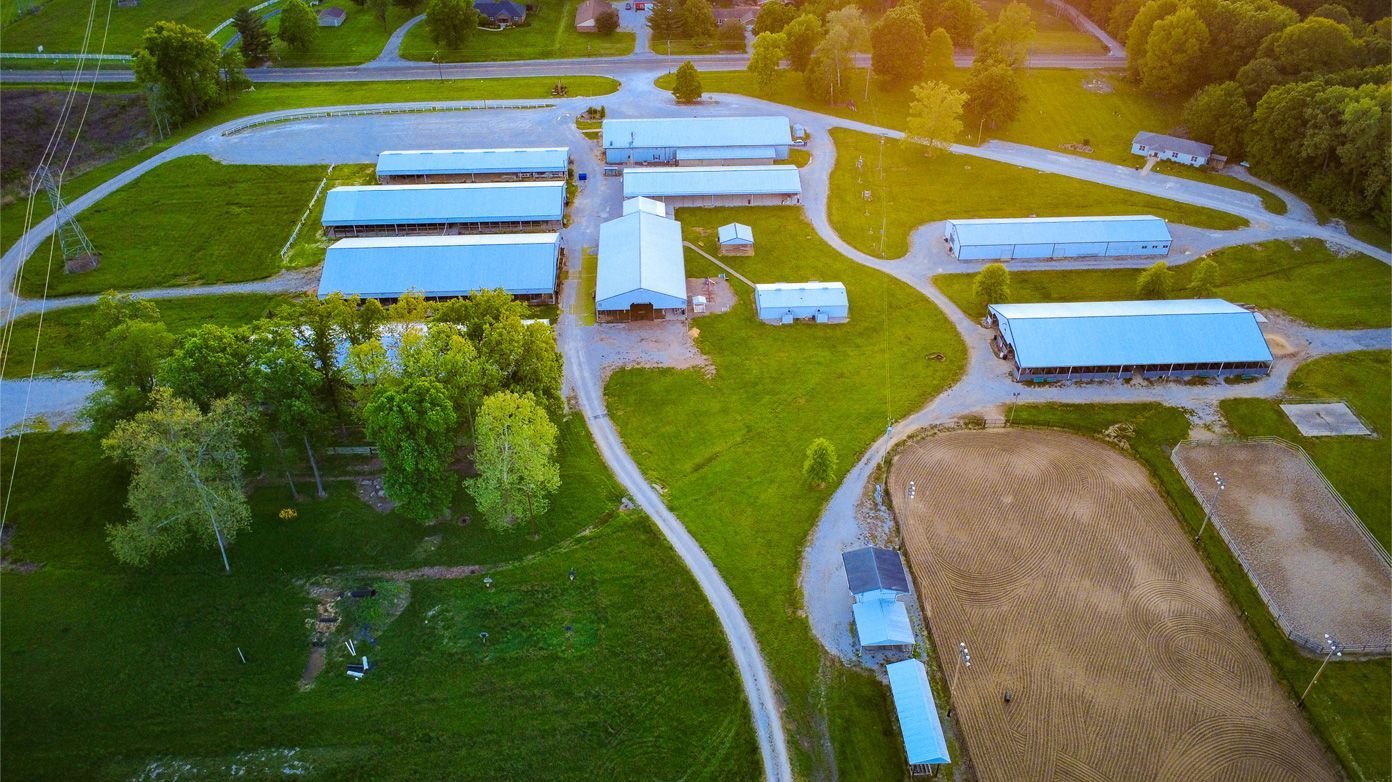 Aerial view of a rural farm with white buildings, silos, winding roads, and fields at sunset