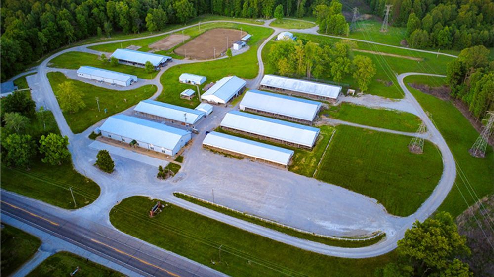 Aerial view of a rural industrial complex with white buildings, roads, and surrounding green trees.