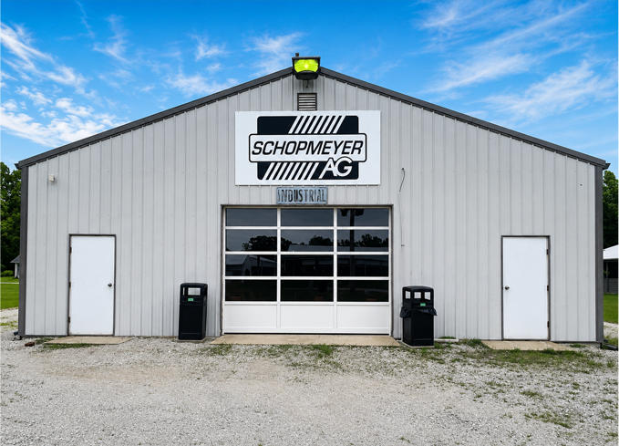 Front view of a gray Shopmeyer AG building with garage doors and gravel lot under a blue sky
