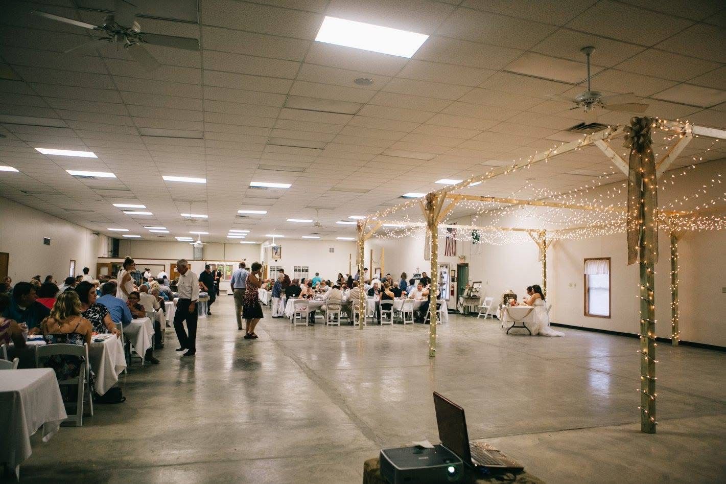Large banquet hall with guests seated at tables and string lights around an open dance floor