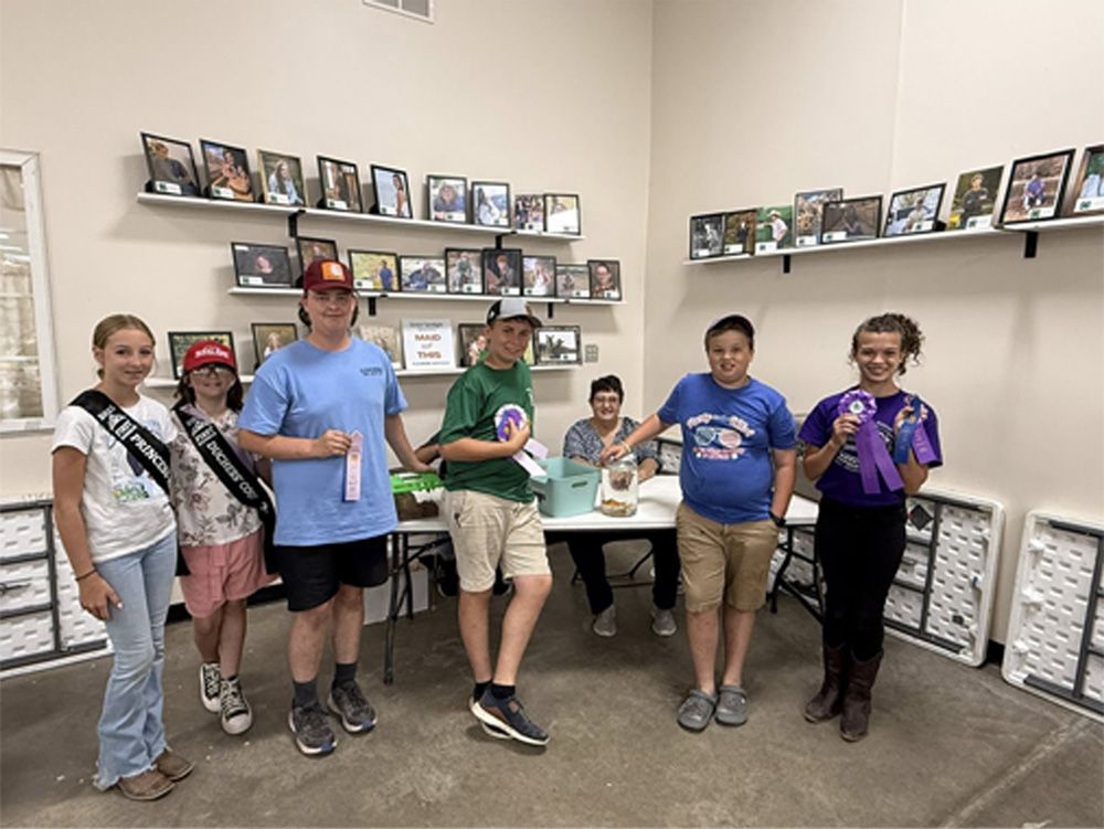 Group holding trophies in a trophy room, standing in front of shelves of framed photos and awards.