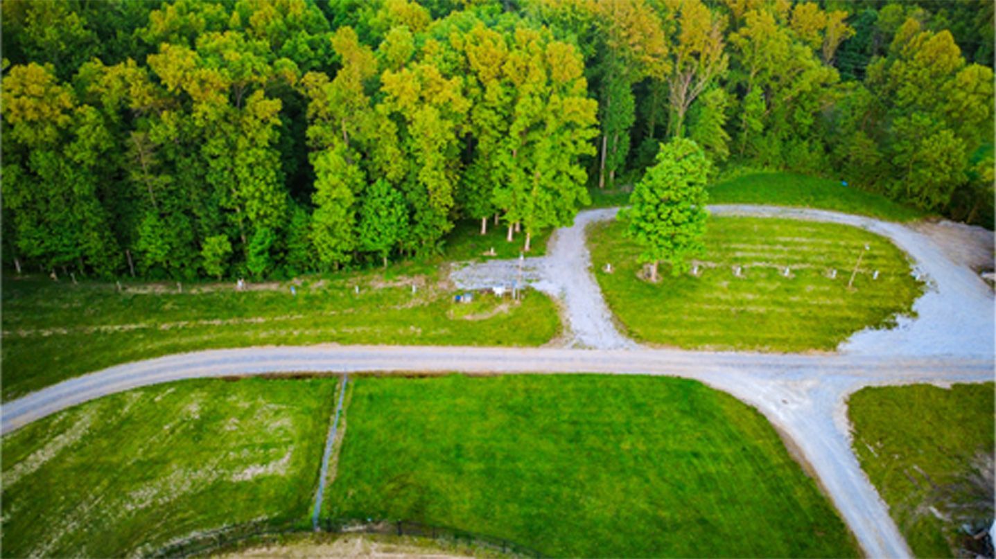 Aerial view of a grassy park with winding paths beside a dense green forest.