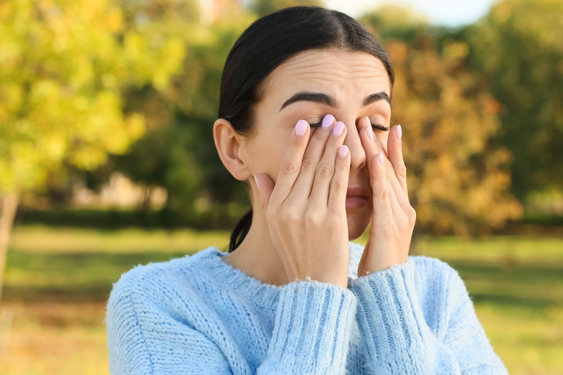woman rubbing eyes because they are itchy from allergies outdoor spring