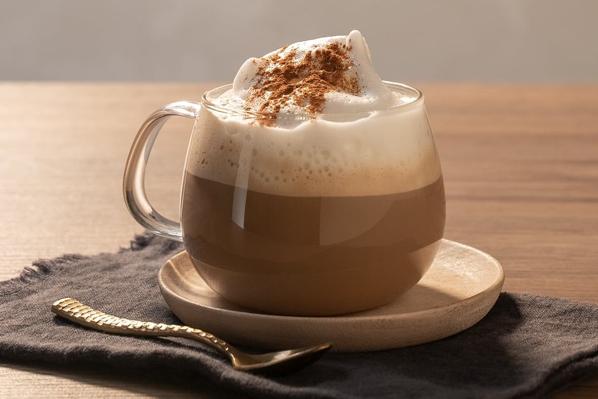 A cup of cappucinno with whipped cream on top is on a saucer on a table.