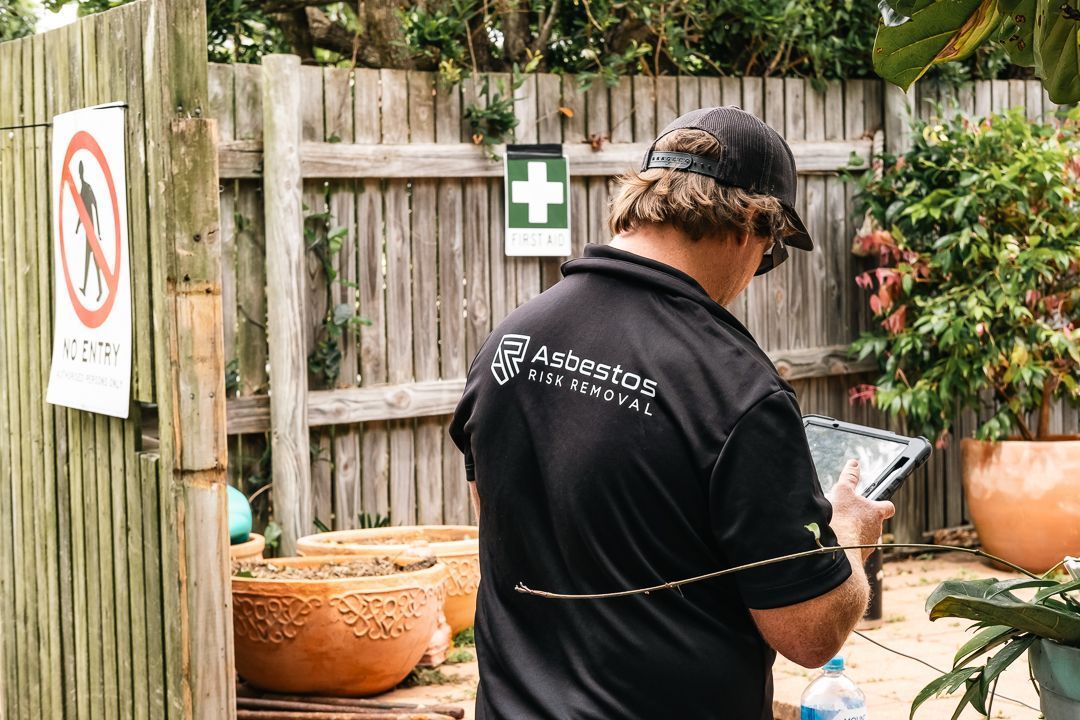 A Person Is Writing on A Clipboard with A Pen — Asbestos Risk Removal In Gladstone, QLD