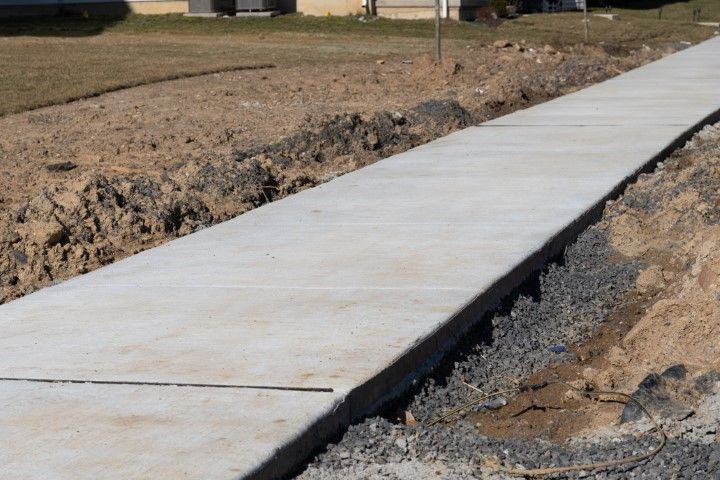 Newly poured concrete sidewalk bordered by dirt and gravel.