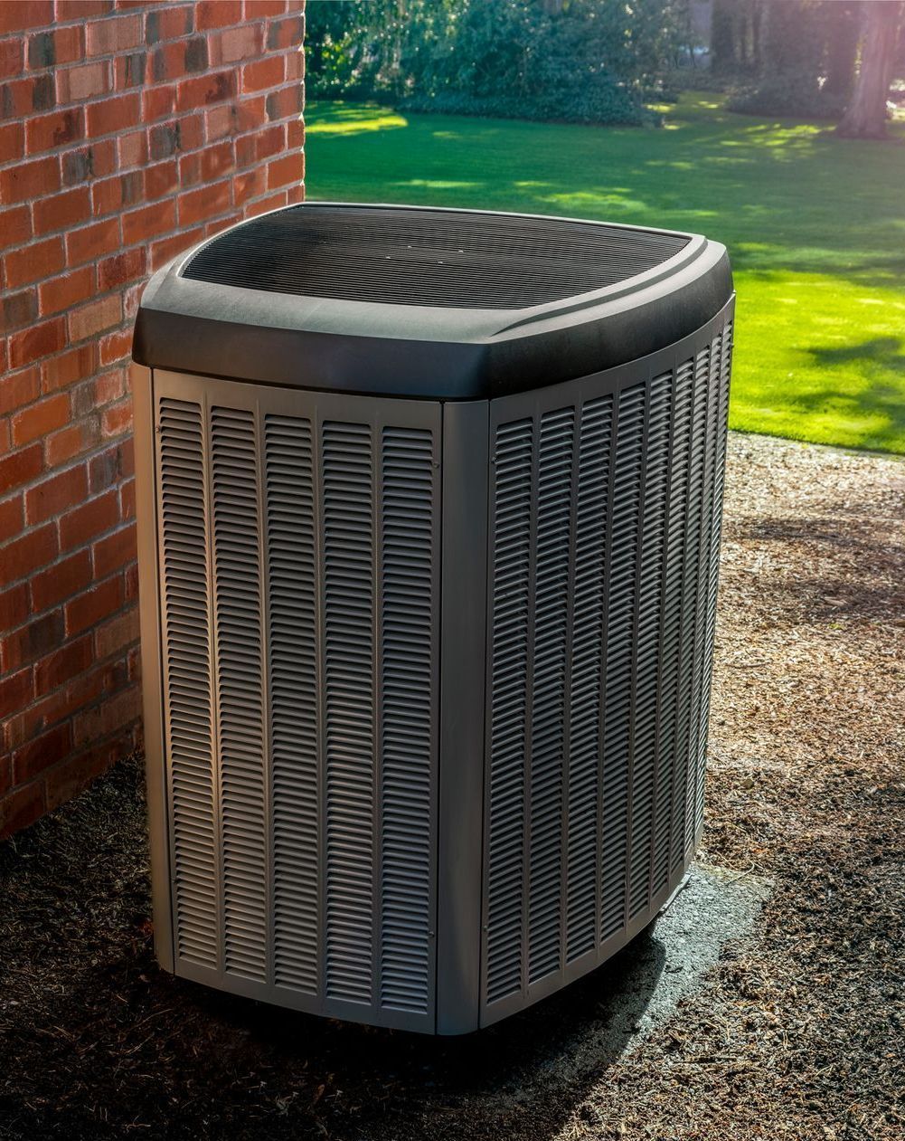Air conditioner unit outside a brick building, on a stone surface.