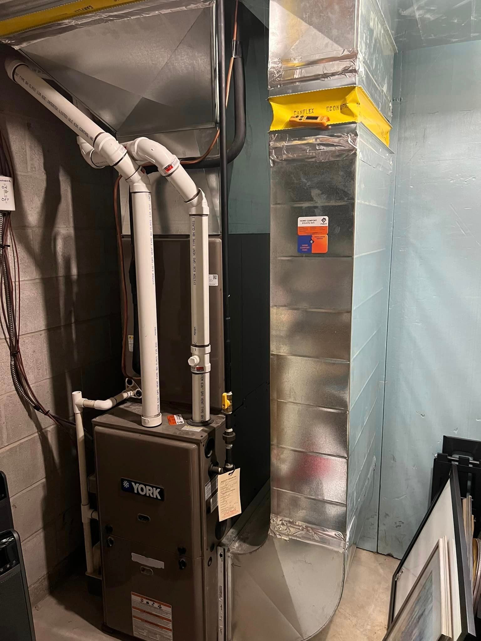 Furnace and ductwork in a basement setting. Metal ducts are silver, furnace is grey, PVC pipes are white.