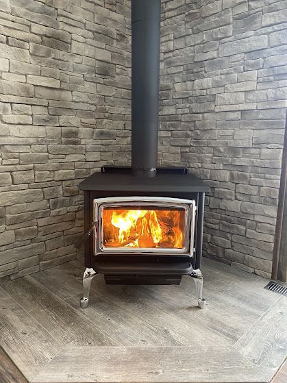 Wood-burning stove with flames, set against a stone wall, on a tiled floor.