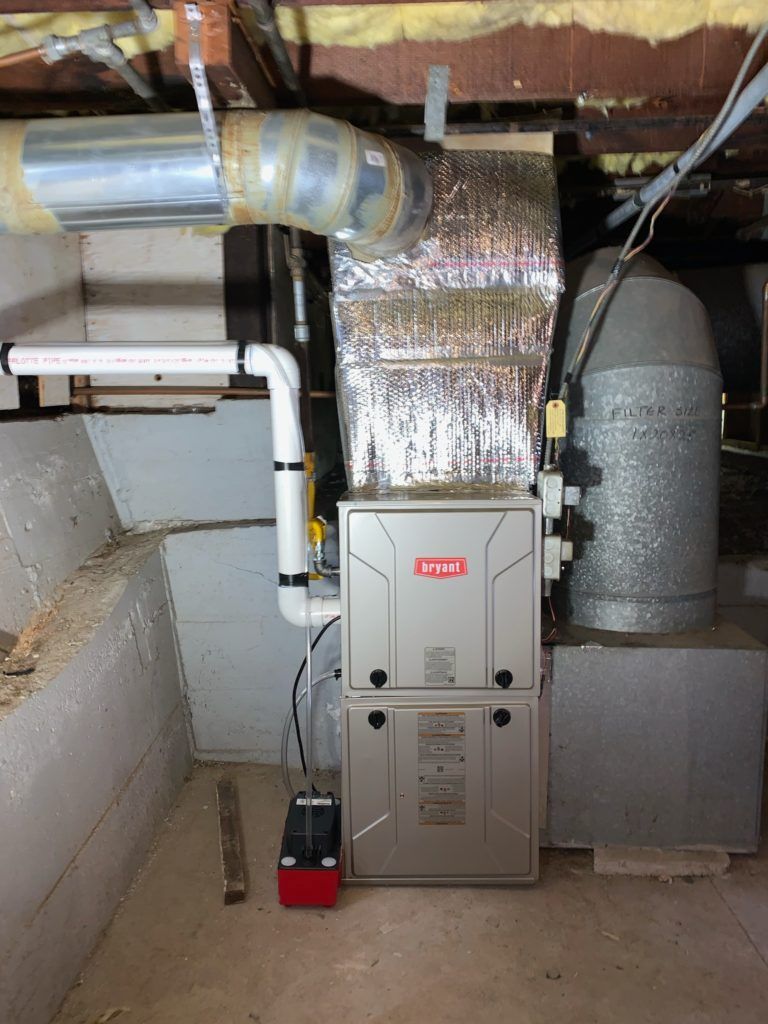 Furnace unit in a basement, with ductwork and a condensate pump.