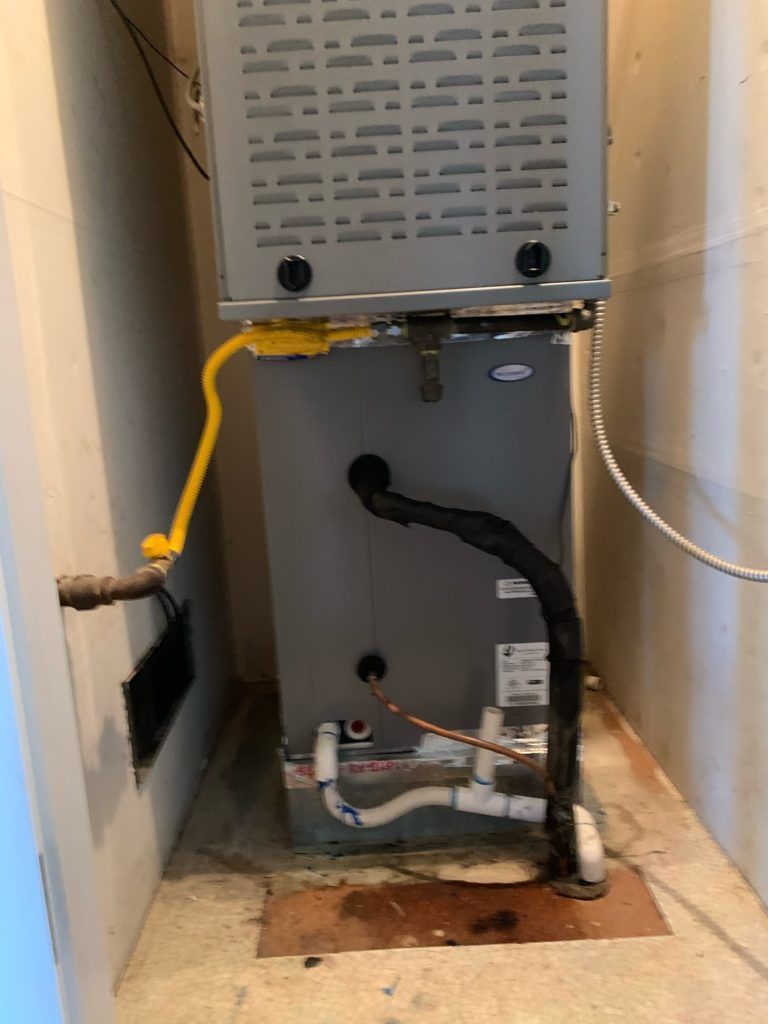 A gas furnace in a recessed space, with ductwork and drainage pipes.