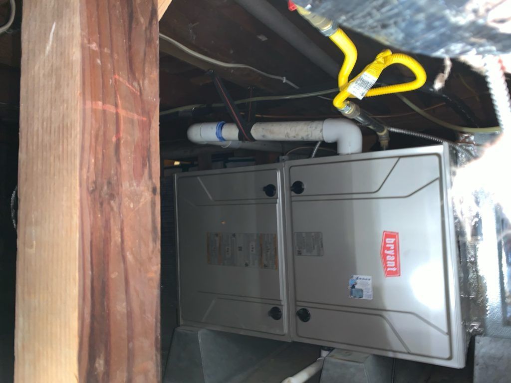 Furnace in a basement, with gas line visible. Silver metal with a red Bryant logo, against wood beam.
