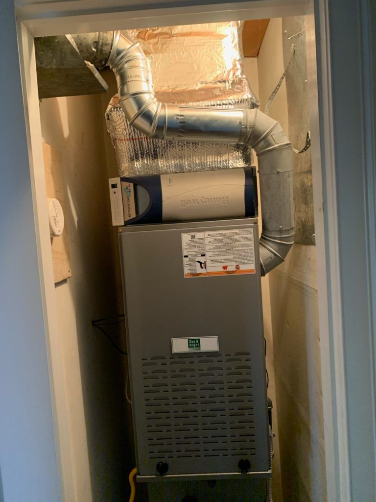 Furnace unit in a closet with ductwork. Silver and gray with insulation.