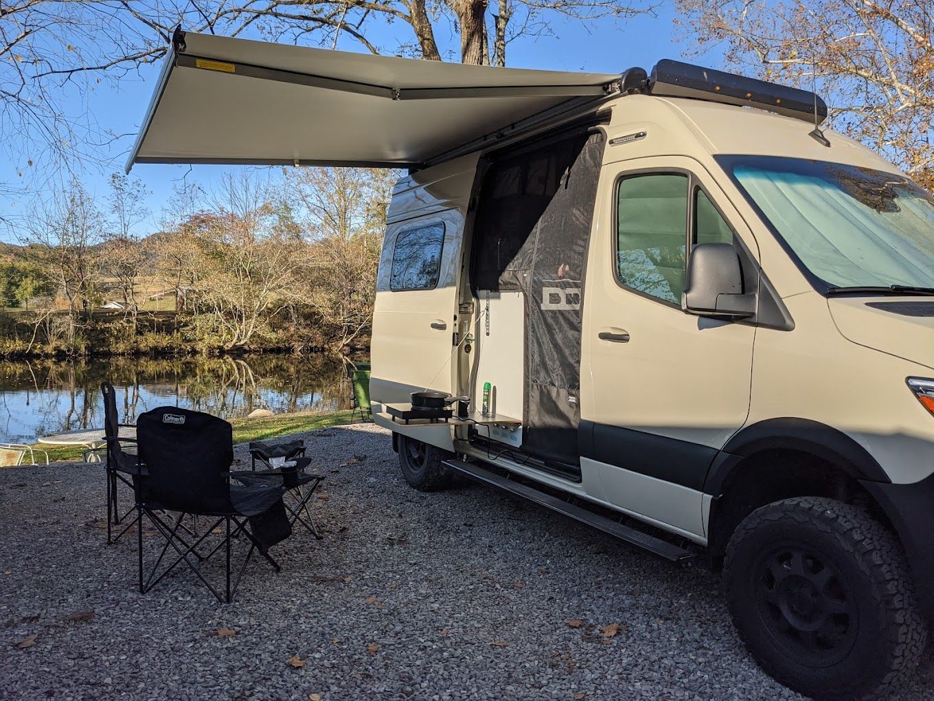 A van with an awning is parked next to a river.