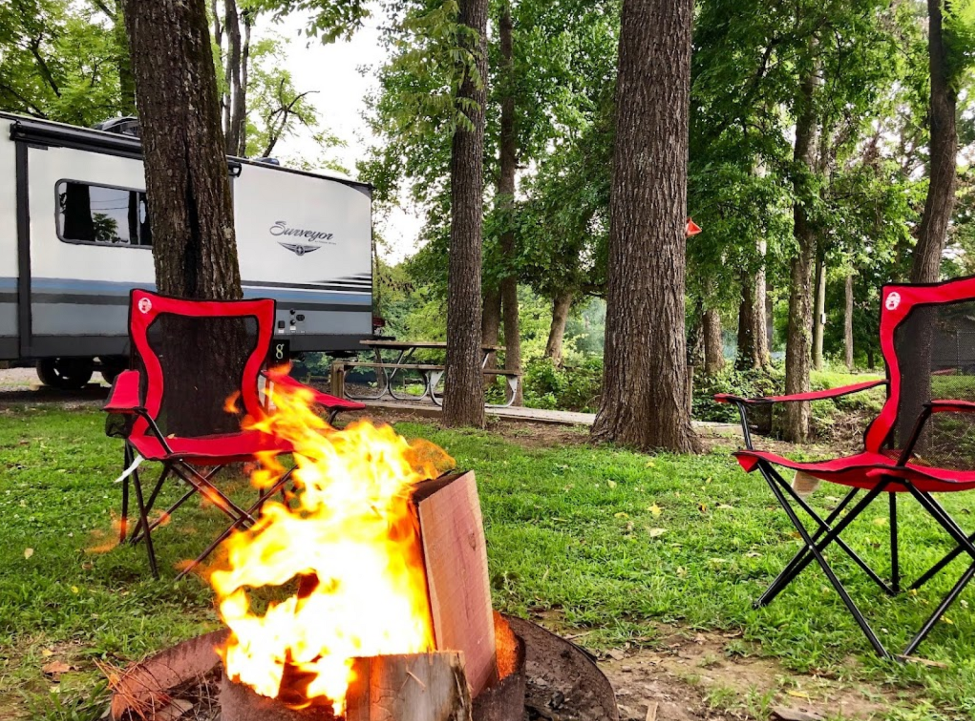 A campfire is sitting in the grass next to a rv.