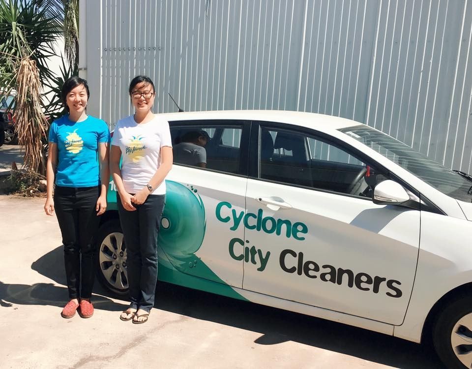 Two People Stand Smiling Next to a White Car — Cyclone City Cleaners In Winnellie, NT