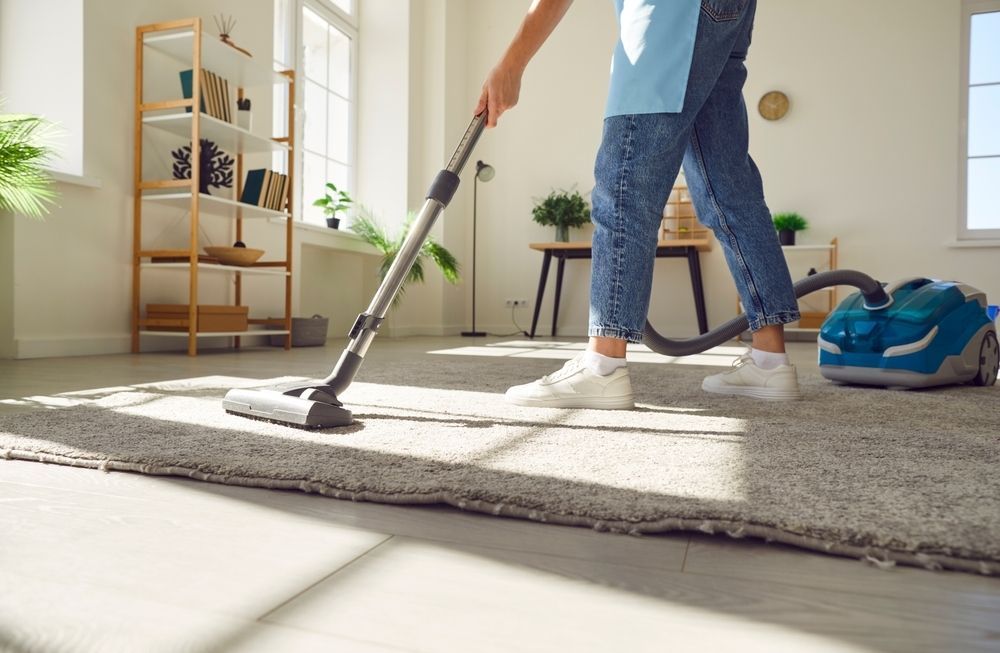 A Person in Blue Jeans Vacuums a Light-colored Rug — Cyclone City Cleaners In Winnellie, NT