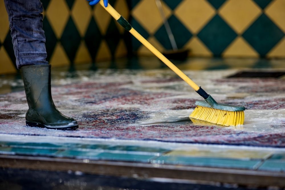 A Person Wearing Rubber Boots Scrubs a Rug — Cyclone City Cleaners In Winnellie, NT