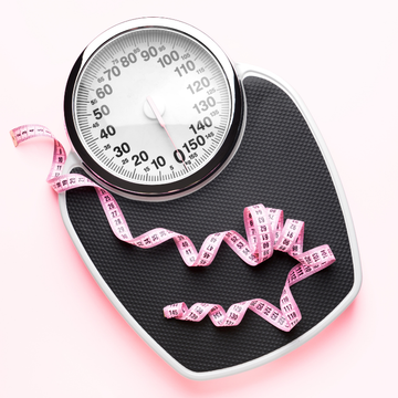 Bathroom scale with pink measuring tape wrapped around it