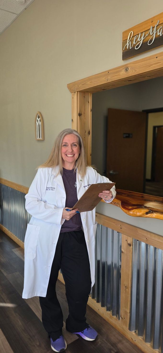 Candace Herrin, APRN, FNP-C stands by a railing, holding a clipboard, smiling.