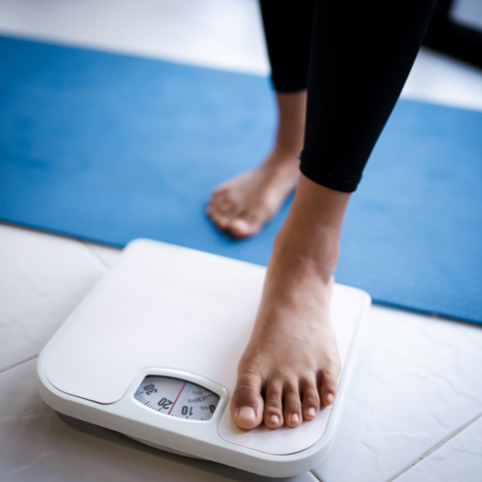 Person stepping on a white digital scale on a blue yoga mat