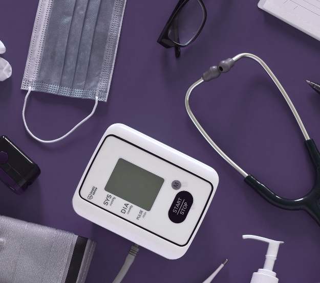 Blood pressure monitor, stethoscope, mask, and sanitizer on a purple background.