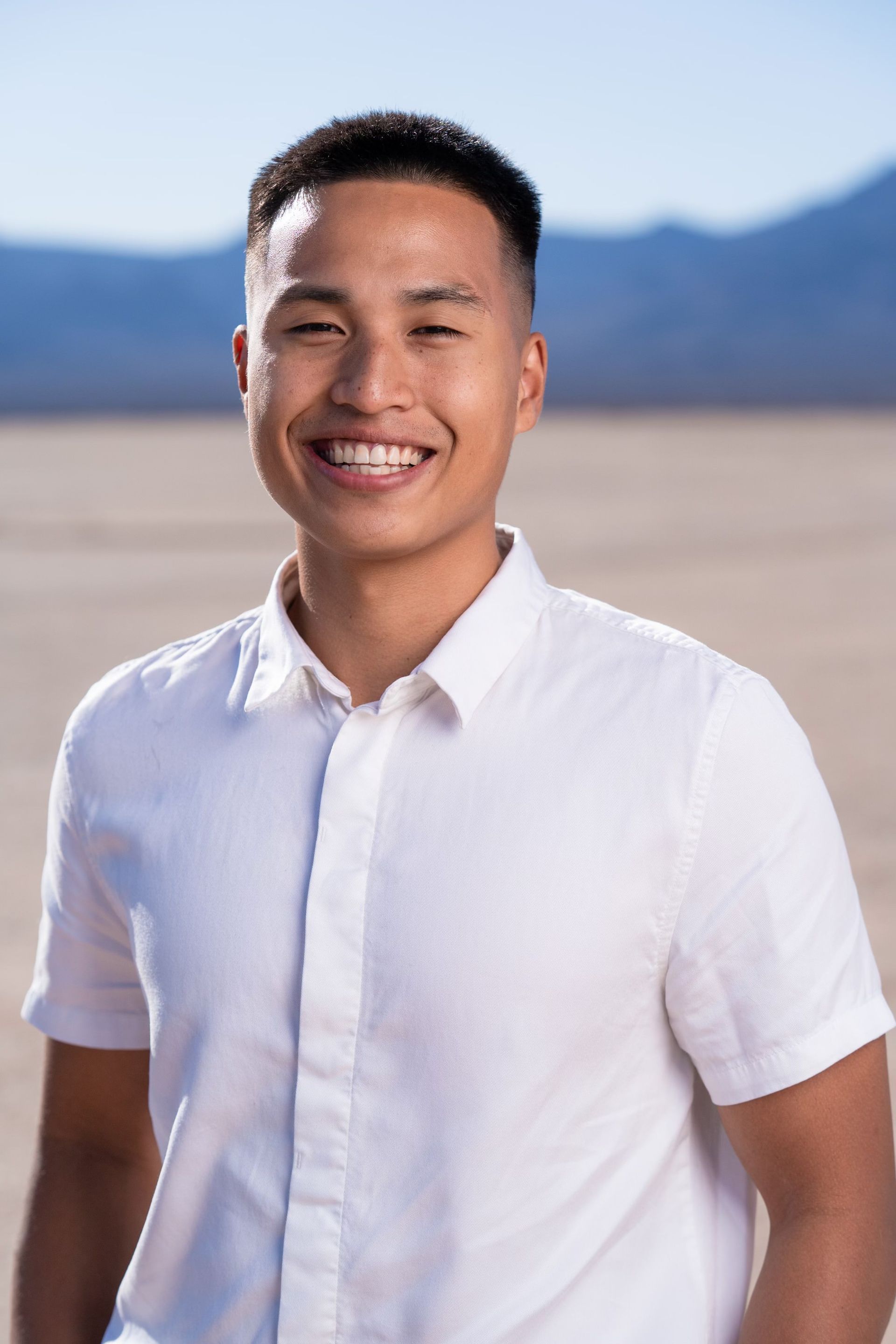 A young man in a white shirt is smiling in the desert.