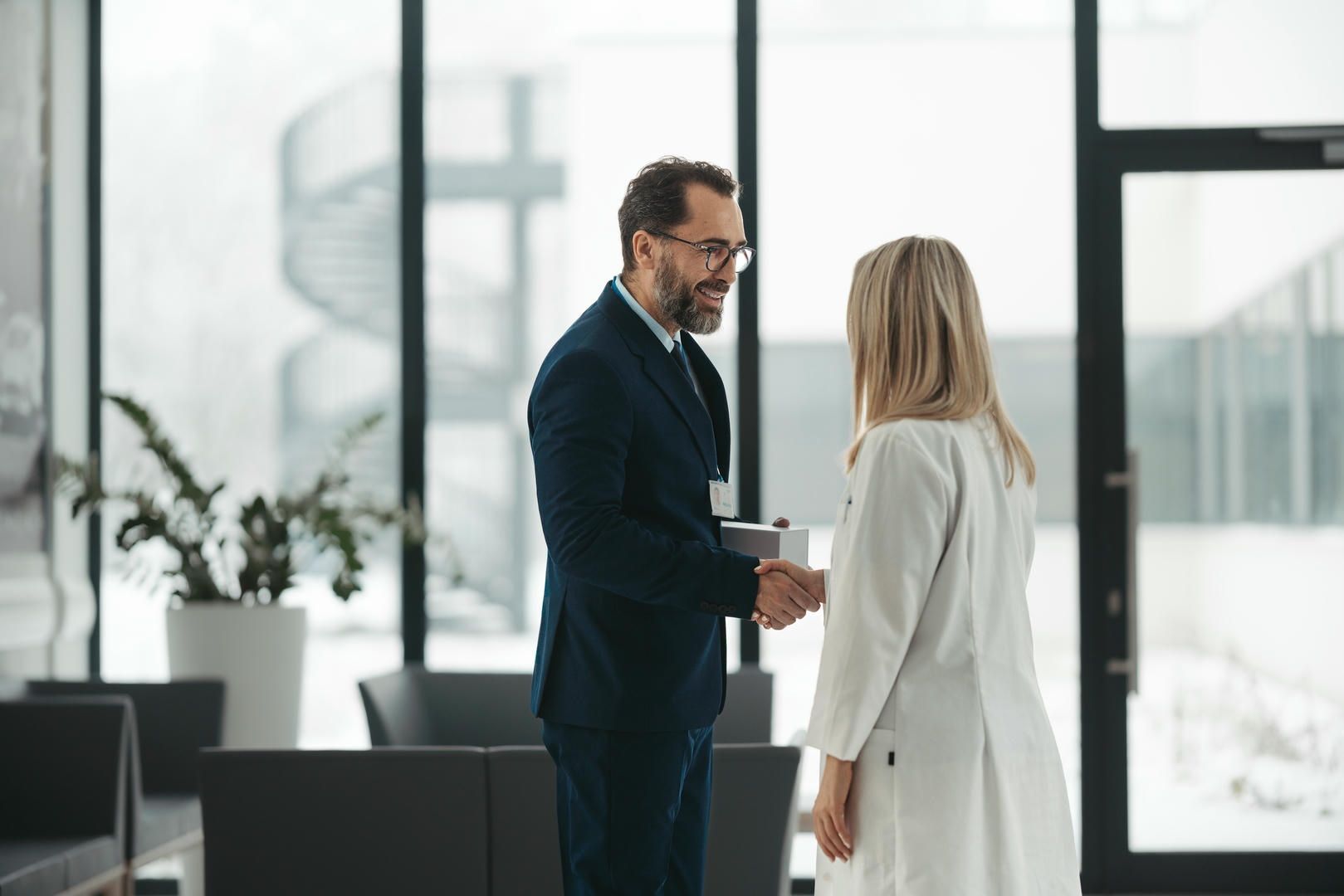 A man in a suit and tie is shaking hands with a woman in a white coat.