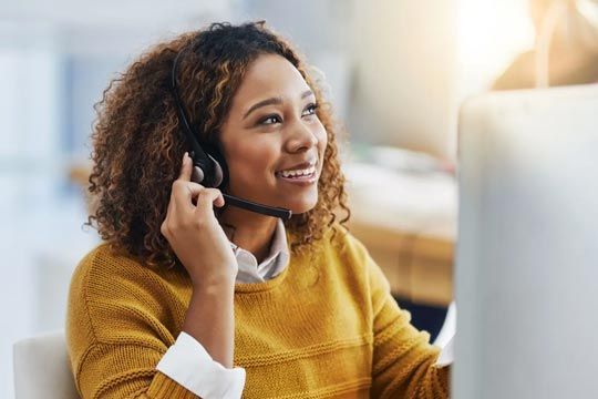 Woman wearing headset, smiling while looking at computer screen in office.
