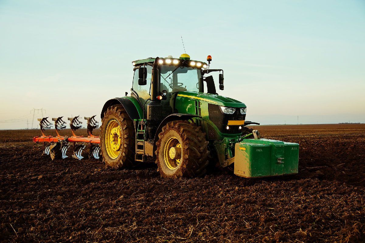 Green tractor plowing a field under a clear sky