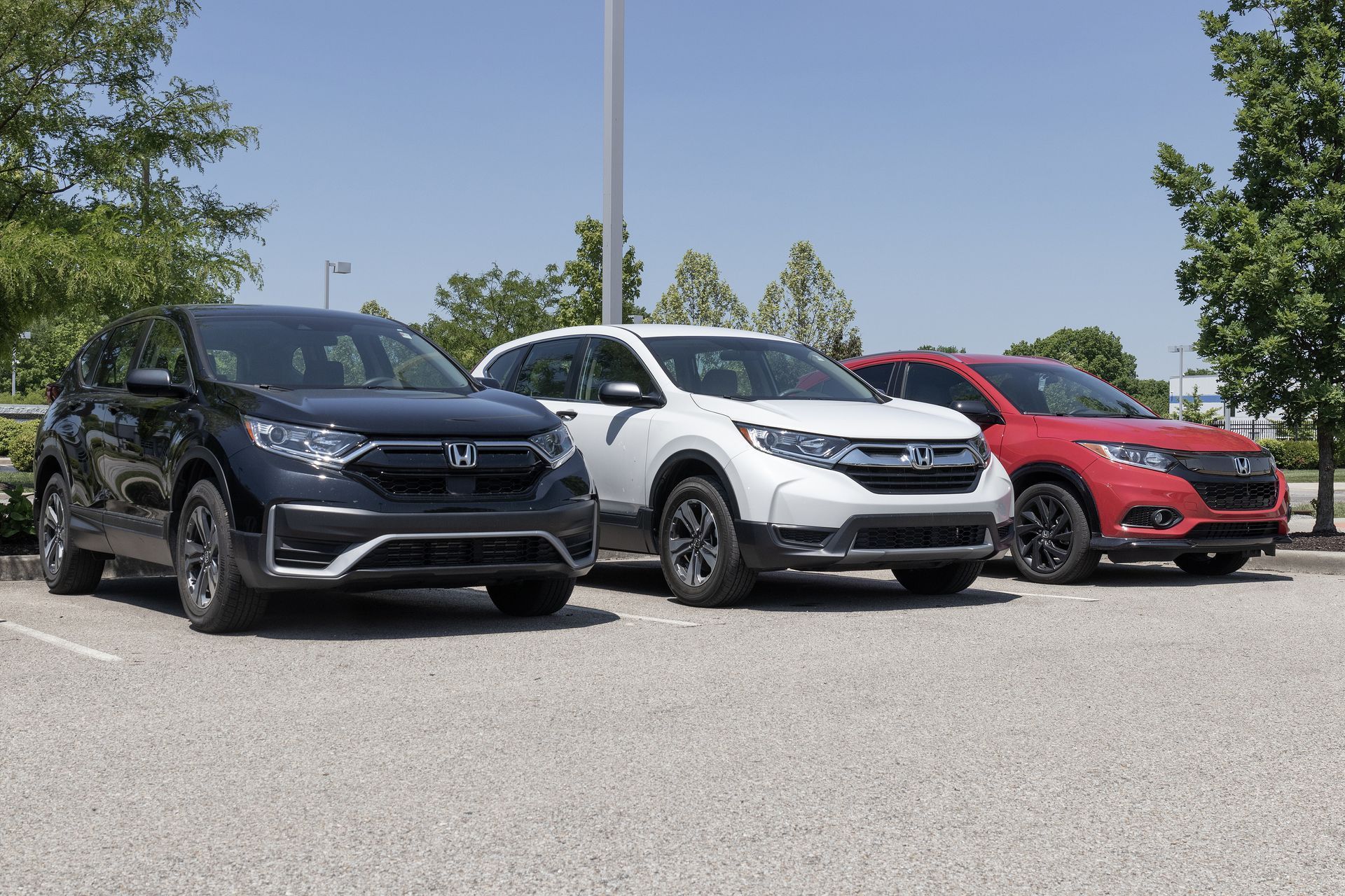 Three SUVs—black, white, and red—parked side by side on a sunny lot.