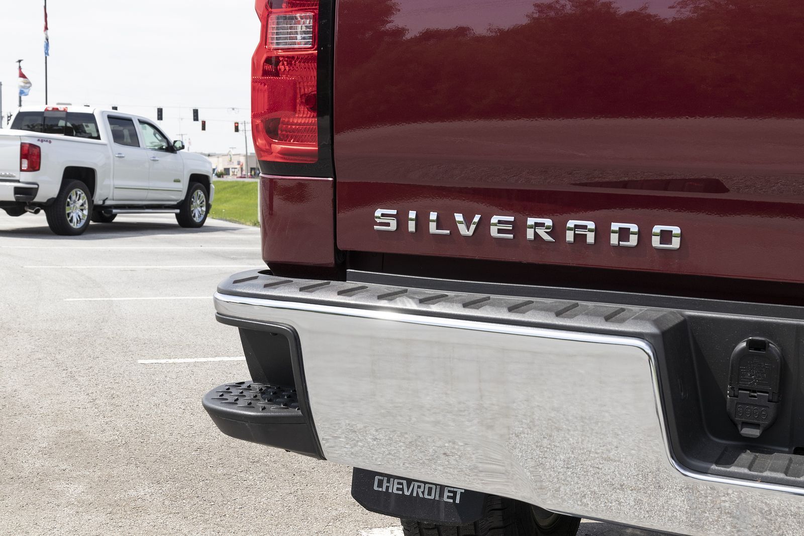 Rear view of a maroon Chevrolet Silverado truck in a parking lot, with a white pickup in the background