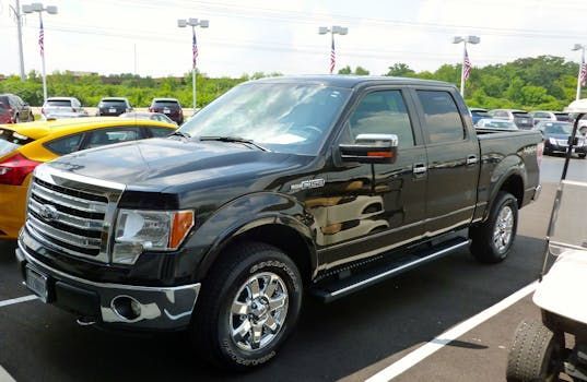 Black Ford pickup truck parked in a dealership lot, side view