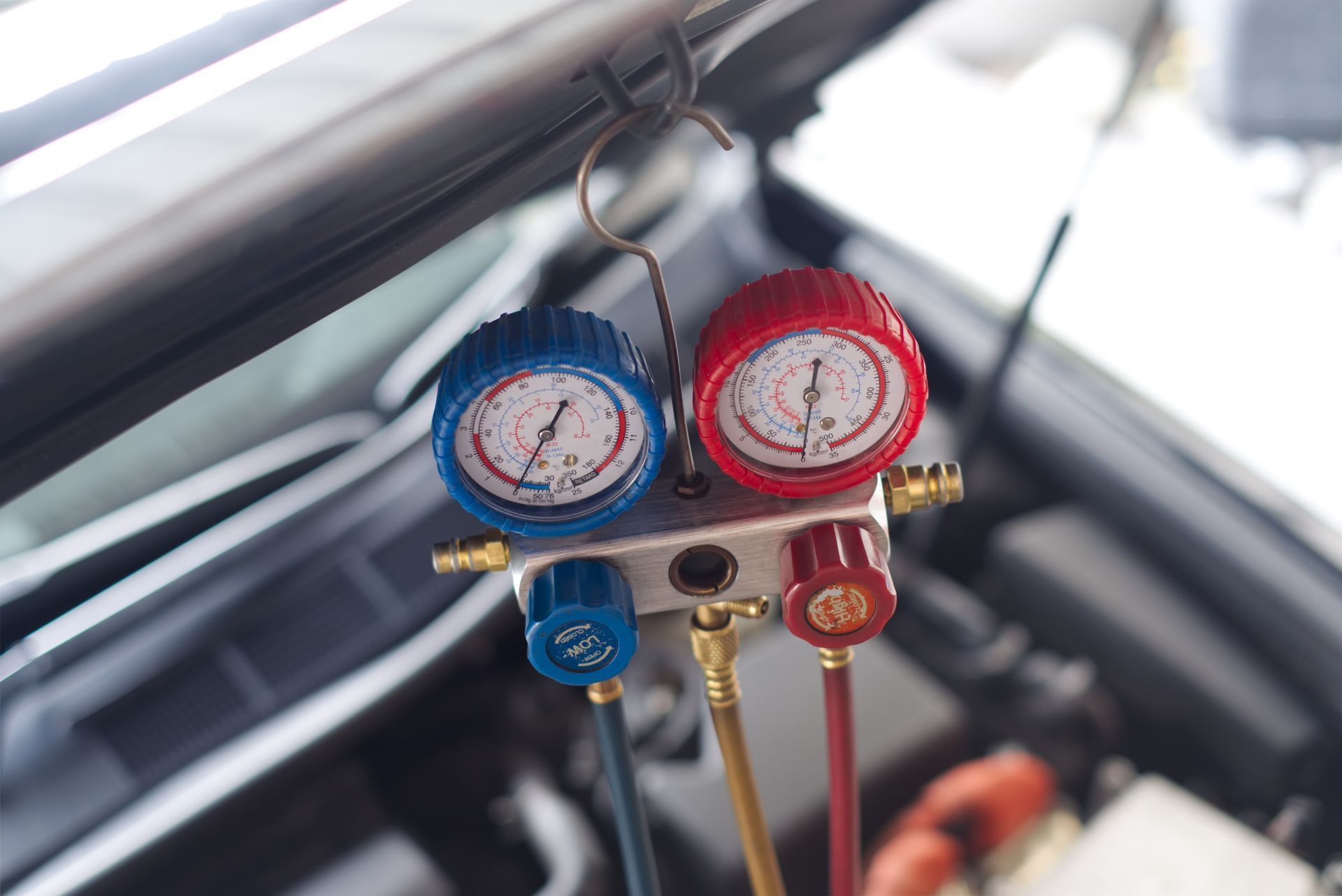 Blue and red automotive gauges on a manifold gauge set, with hoses attached in a car engine bay
