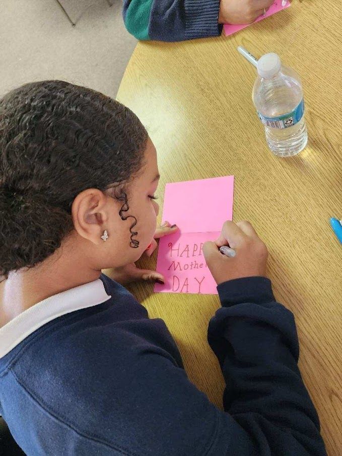 A girl is sitting at a table writing on a piece of pink paper.