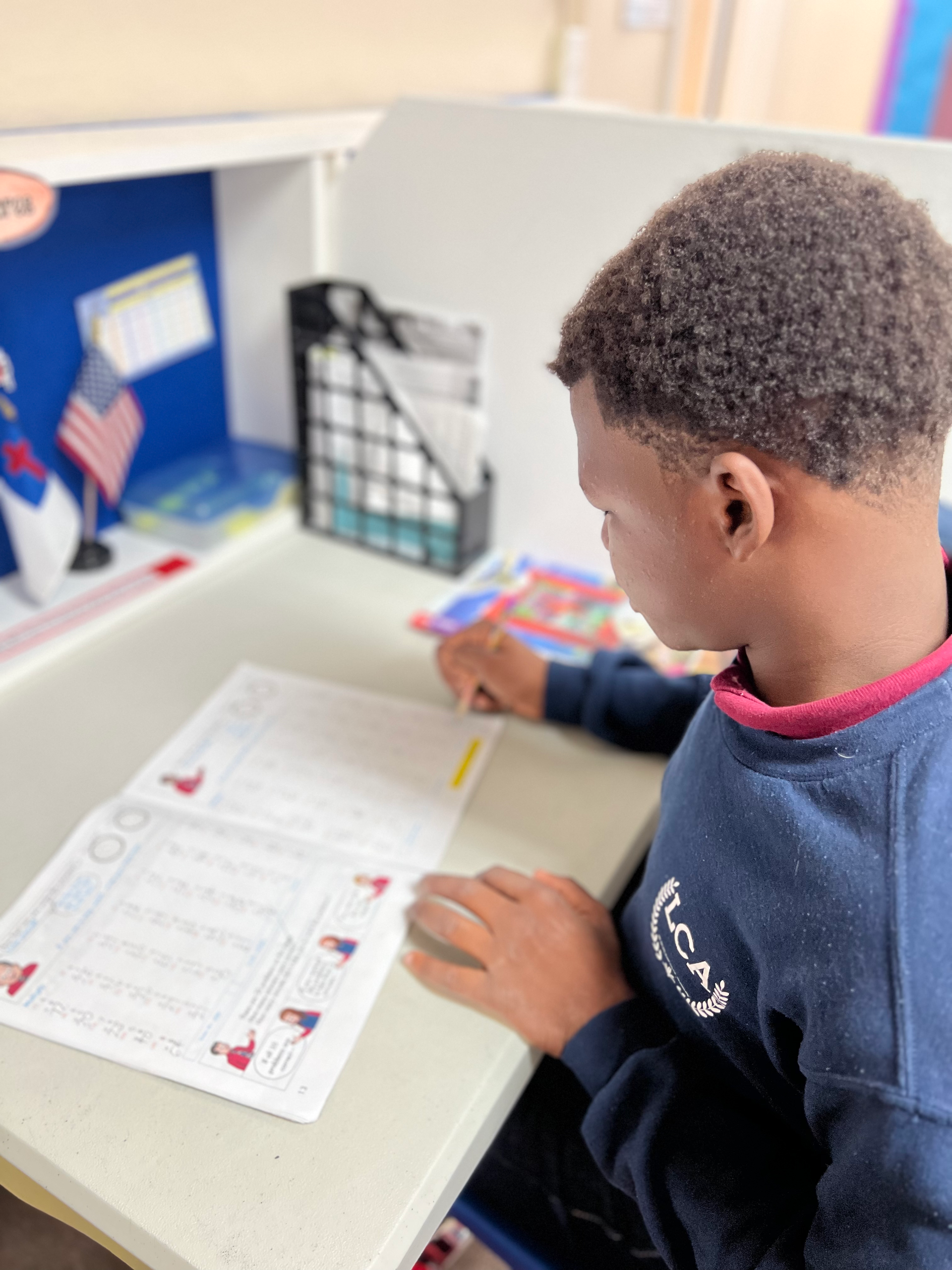 A young boy is sitting at a desk writing on a piece of paper