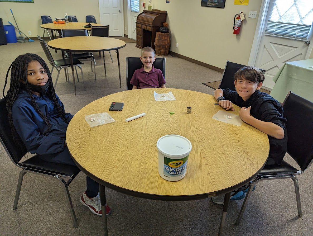 Three children are sitting at a round table in a room.
