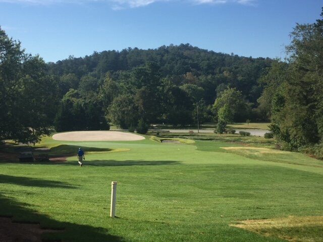 Golf course fairway with sand bunker, green trees, and a blue sky