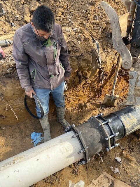 Worker standing by a large pipe repair at a muddy trench site