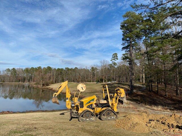 Yellow backhoe by a lake on a dirt road under a blue sky