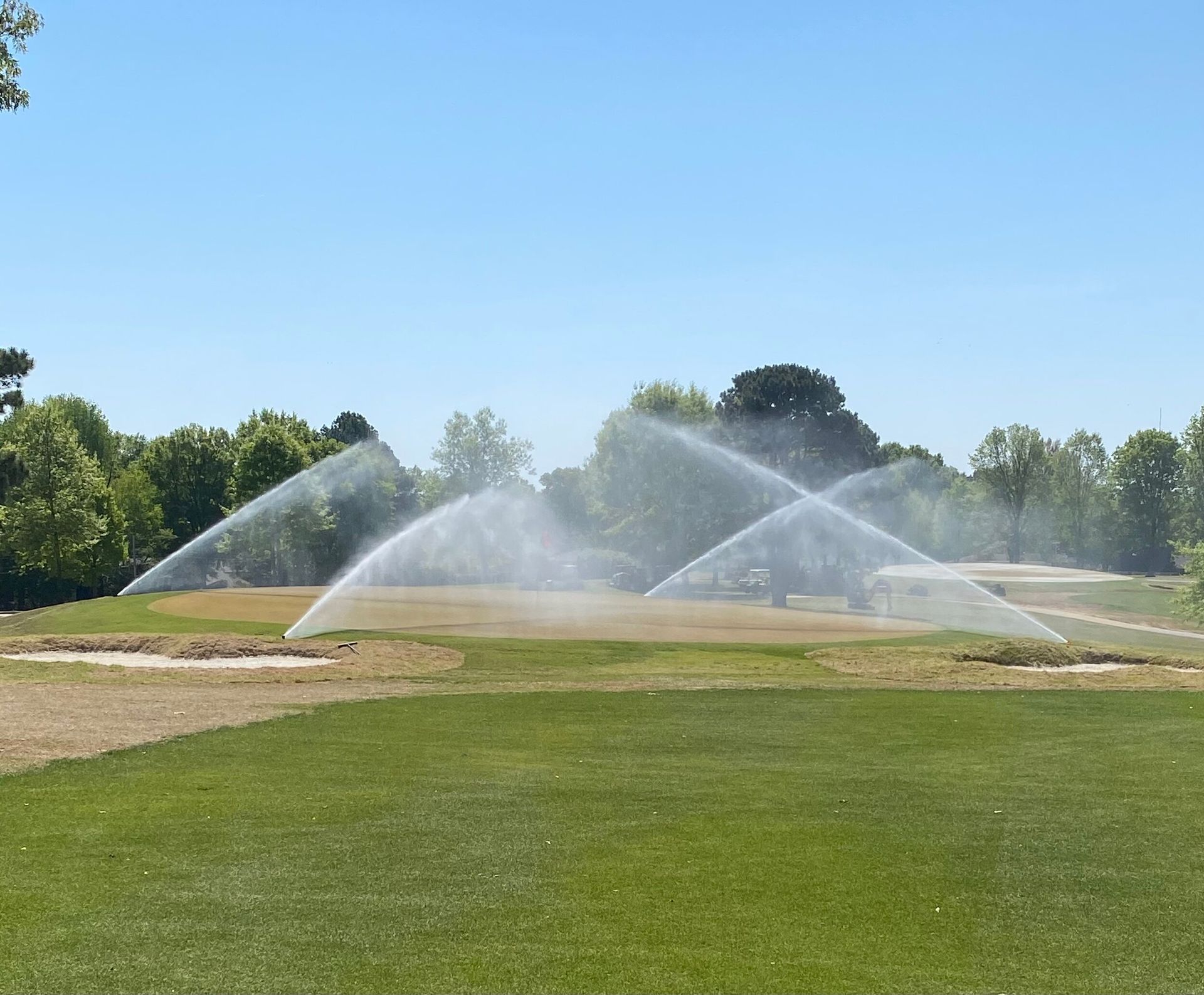 Water sprinklers arching over a green lawn on a sunny day