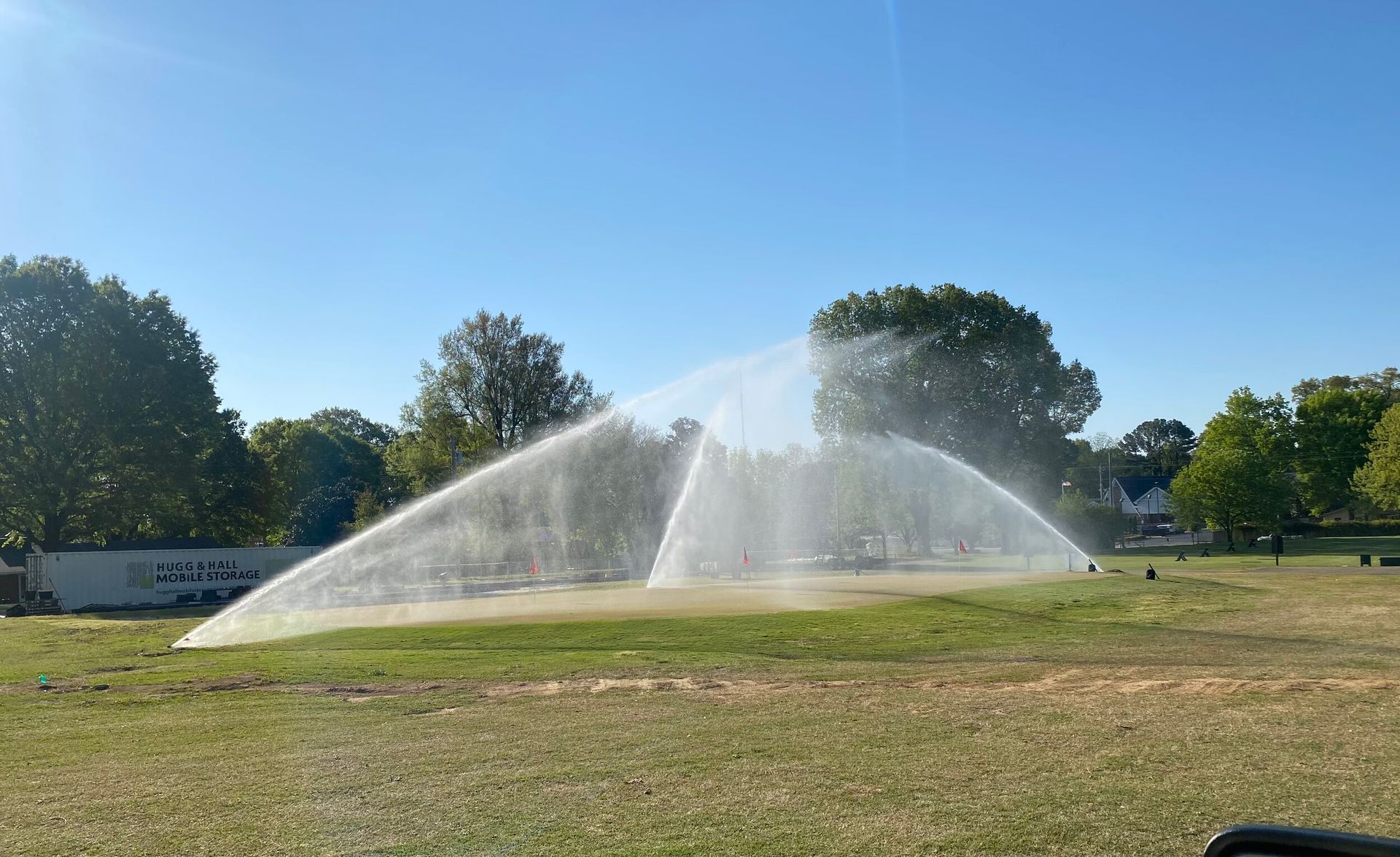 Sprinklers spraying water across a sunny park field under a clear blue sky