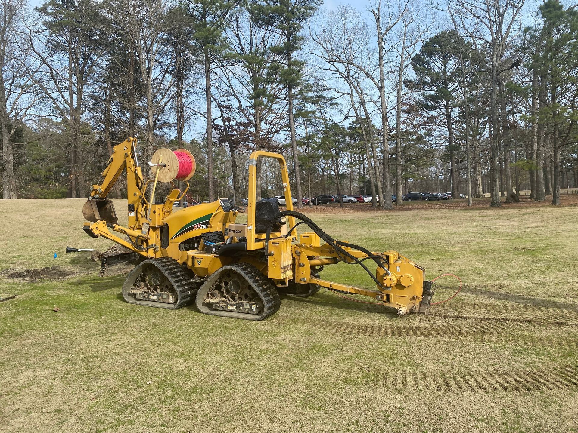 Yellow tracked drilling machine on a grassy field with trees in the background