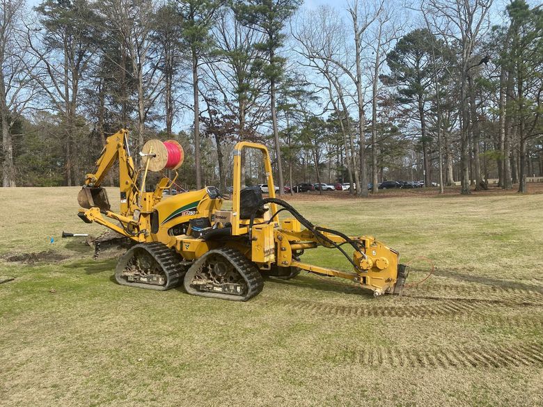 Yellow tracked utility machine with a front attachment on a grassy field near trees