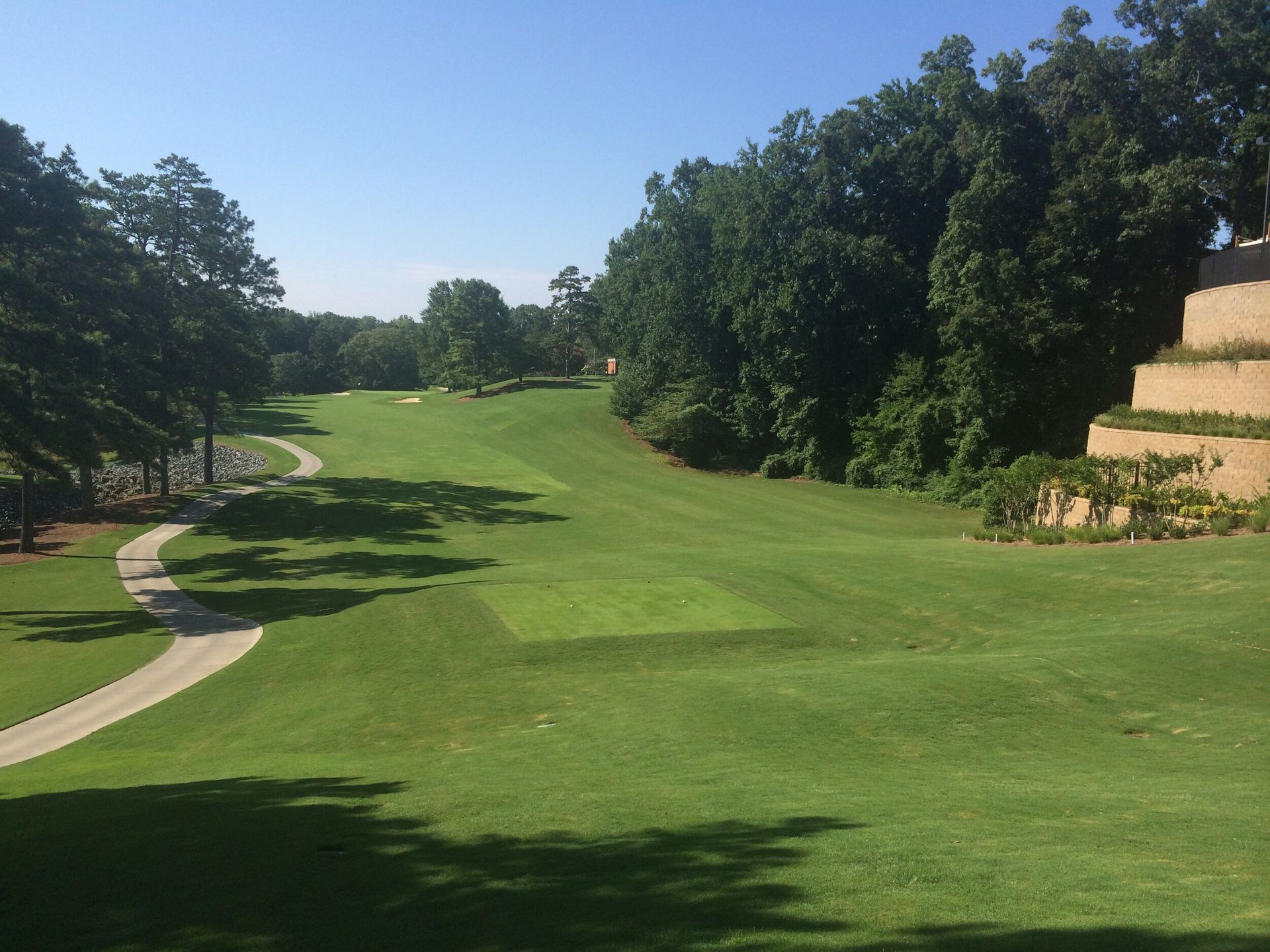 Wide green golf course fairway with trees, a winding path, and a clear blue sky