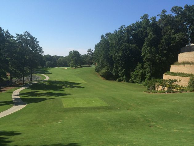 Sunny golf course fairway lined with trees and a cart path on the left