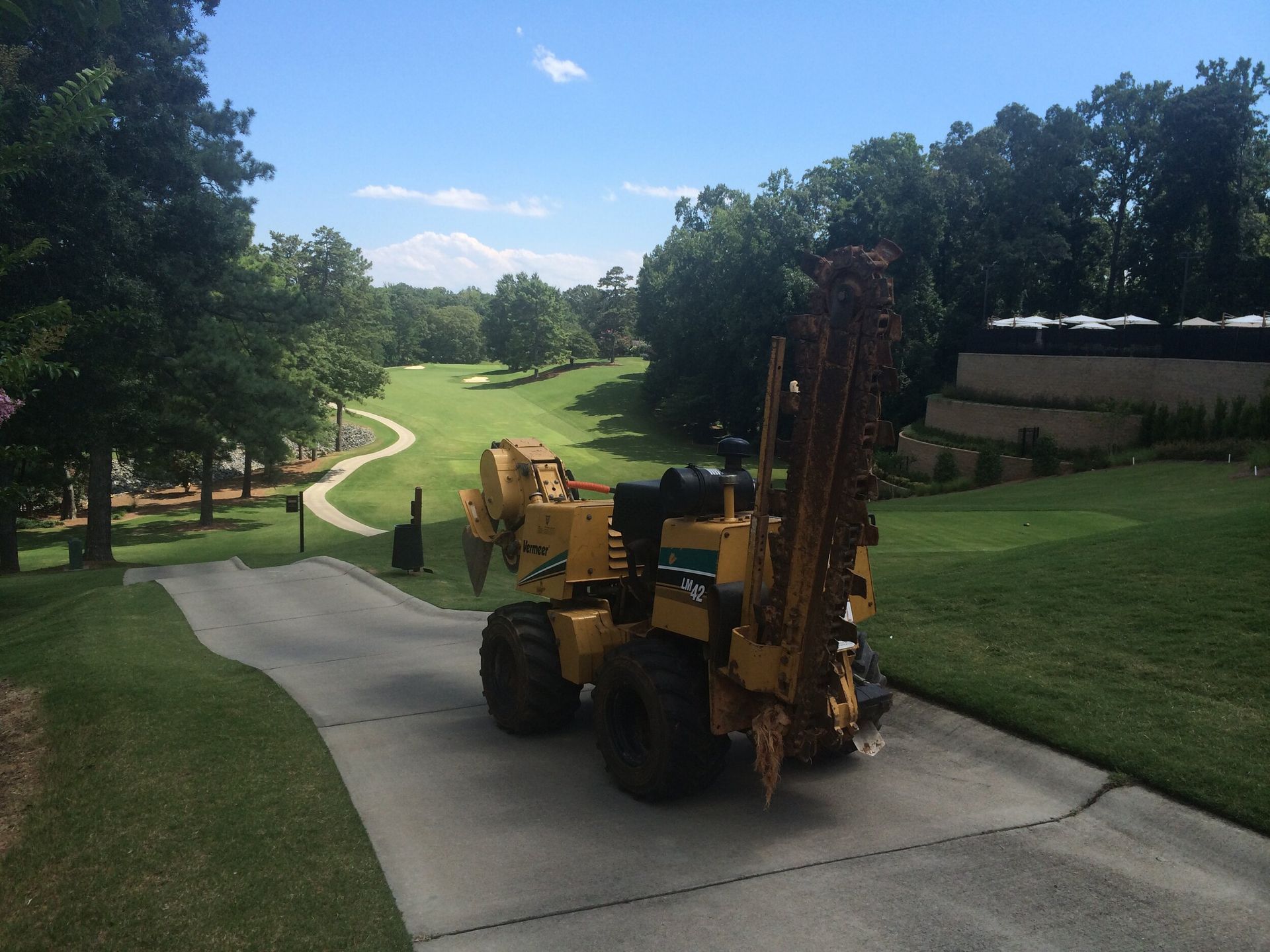 Yellow utility truck on a paved path in a grassy park, carrying tall equipment.