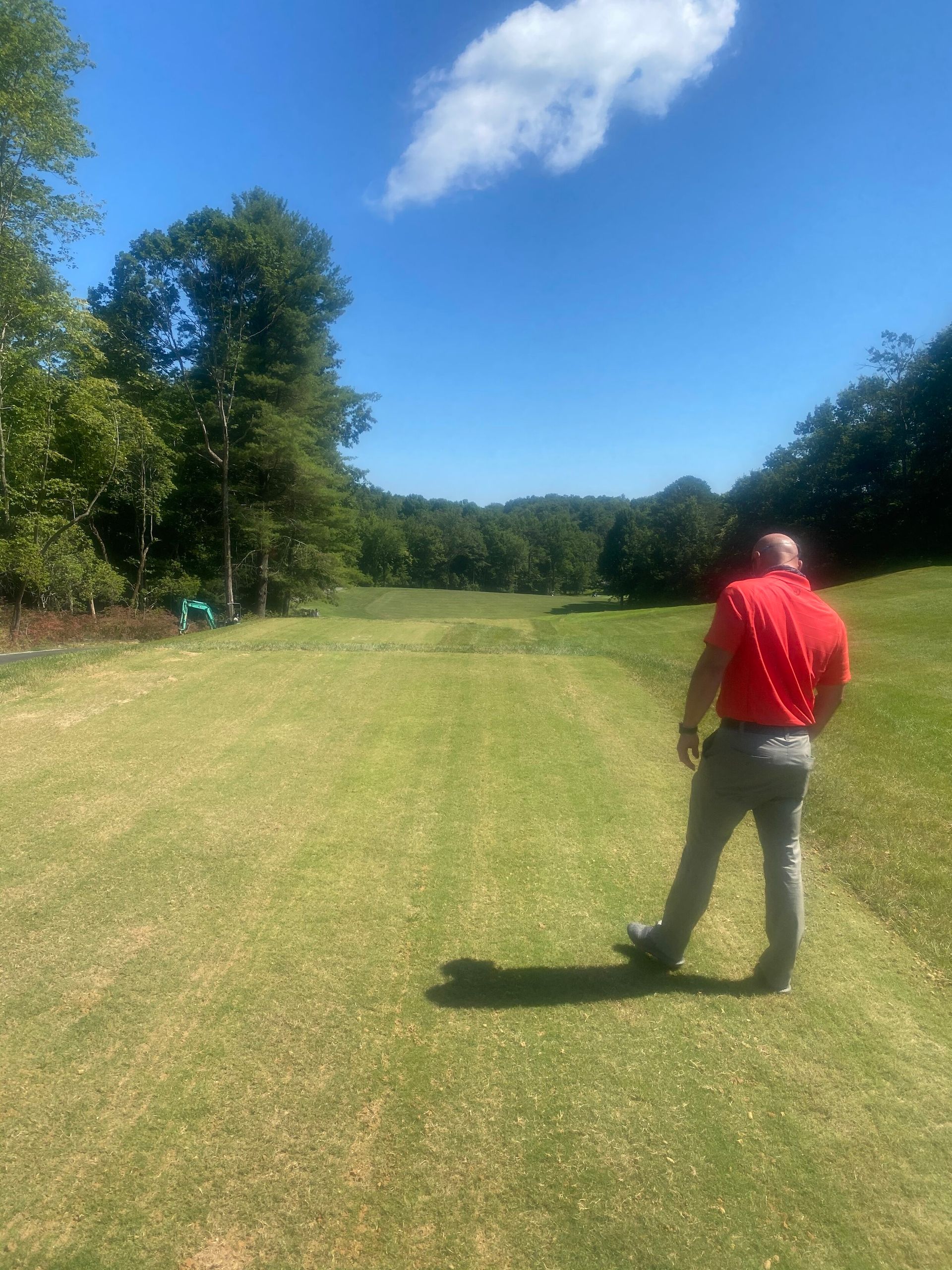 Person in red shirt standing on a grassy field under a bright blue sky.
